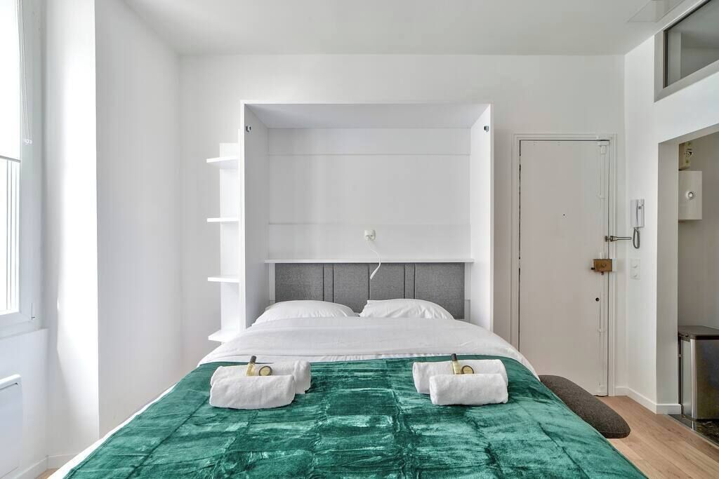 A modern bedroom with a bed, a green textured bedspread, and two towels on the bed.