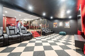 A cinema room with black leather recliners, a checkered floor, red velvet ropes, and posters on the wall.