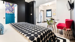 A modern hotel room with a bed, a red chair, a small table, and a wall-mounted TV.