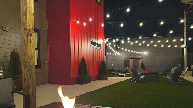 A backyard with a fire pit, outdoor seating, string lights, and a red building.