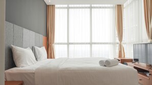 A hotel room with a large bed, a flat-screen TV, and a large window with curtains. - Elegant And Spacious 3Br At Ciputra International Apartment (Jakarta)