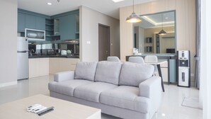 A modern living room with a grey sofa, a coffee table, and a dining area with a table and chairs. - Elegant And Spacious 3Br At Ciputra International Apartment (Jakarta)