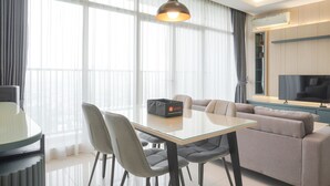 A modern living room with a glass dining table, grey sofas, and a large flat-screen TV. - Elegant And Spacious 3Br At Ciputra International Apartment (Jakarta)