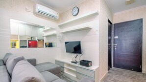 A modern living room with a grey sofa, a flat-screen TV, and built-in shelves. - Elegant And Comfortable 1Br Apartment At Atlanta Residences (Depok)