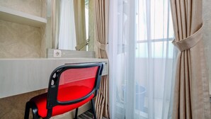 A hotel room with a bed, a desk with a chair, a window with curtains, and a mirror. - Elegant And Comfortable 1Br Apartment At Atlanta Residences (Depok)