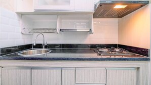 A kitchen with a stainless steel sink, black granite countertop, white cabinetry, and a gas stove. - Elegant And Comfortable 1Br Apartment At Atlanta Residences (Depok)