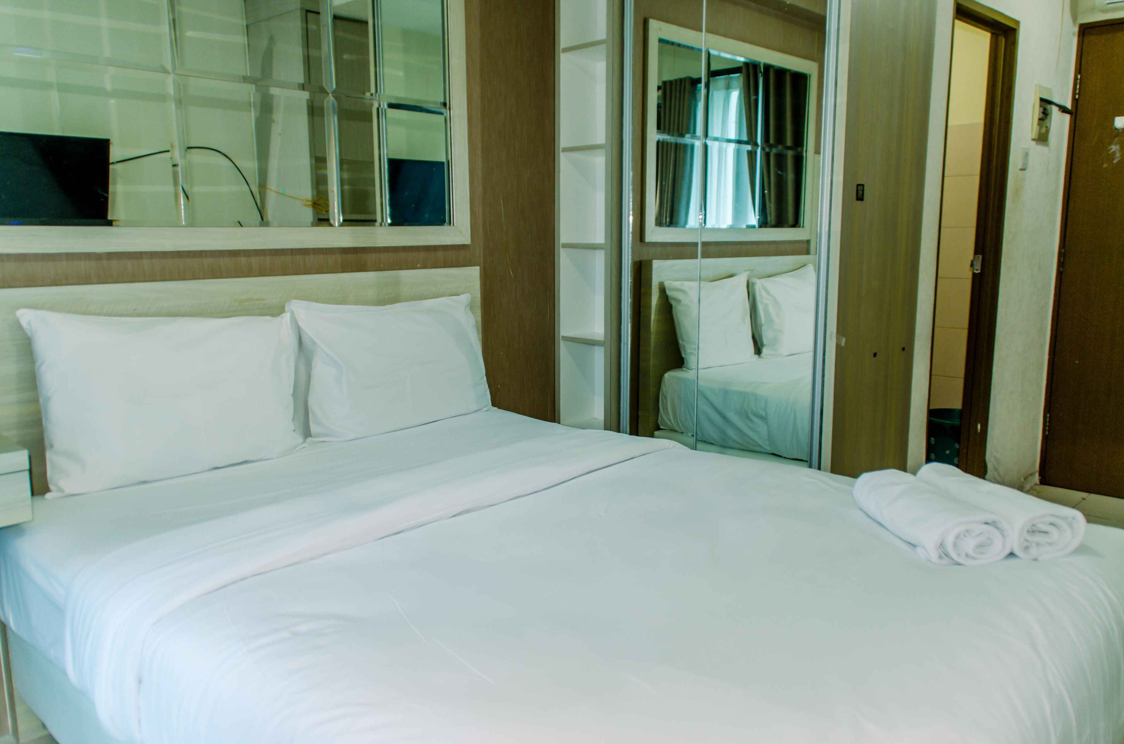Una habitación de hotel con una cama grande, ropa de cama blanca, un espejo y una puerta que da a un baño.