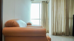 Una habitación con dos sofás anaranjados, un ventanal con cortinas y un televisor a la derecha.