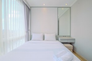 A modern hotel room with a large bed, a bedside table, a mirror, and a window with sheer curtains. - Elegant And Comfy 2Br At Menteng Park Apartment (Jakarta)