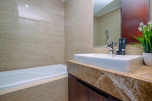 A modern bathroom with a large bathtub, a sink with a marble countertop, and a mirror above the sink. - Elegant And Comfy 2Br At Menteng Park Apartment (Jakarta)