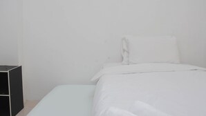 A single bed with white bedding in a room with white walls and a black storage unit. - Cozy Stay And Homey Studio At Tifolia Apartment (Jakarta)
