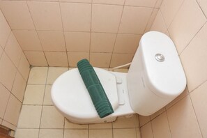 Des toilettes avec une serviette verte posée sur le siège et un bouton de chasse d’eau blanc.