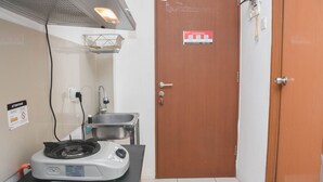 A compact kitchen with a gas stove, sink, and a door with a sign. - Cozy Stay And Homey Studio At Tifolia Apartment (Jakarta)