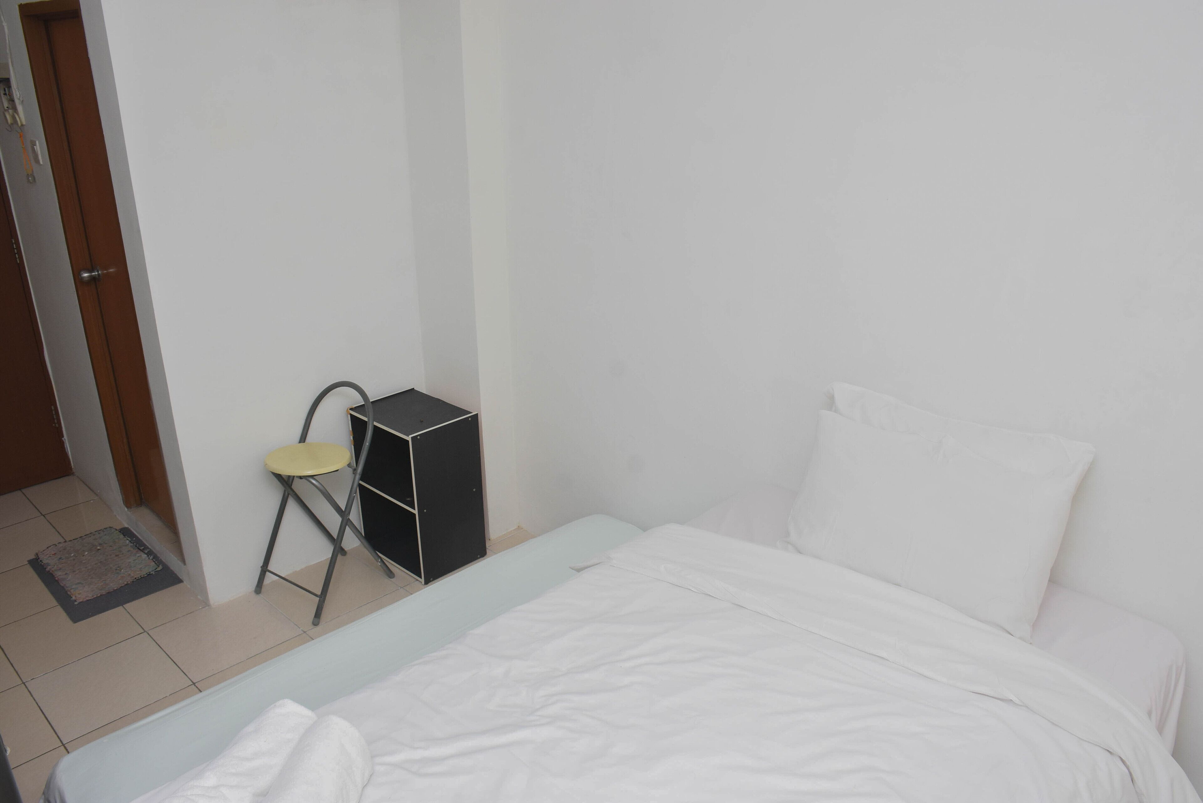 Una habitación pequeña y limpia, con cama, una silla y un escritorio.