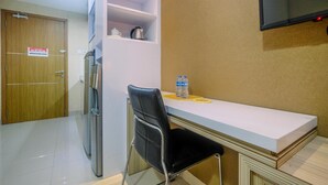 A small kitchenette with a refrigerator, a microwave, and a coffee maker on the counter. There is a chair and a table with a bottle of water and a plate.