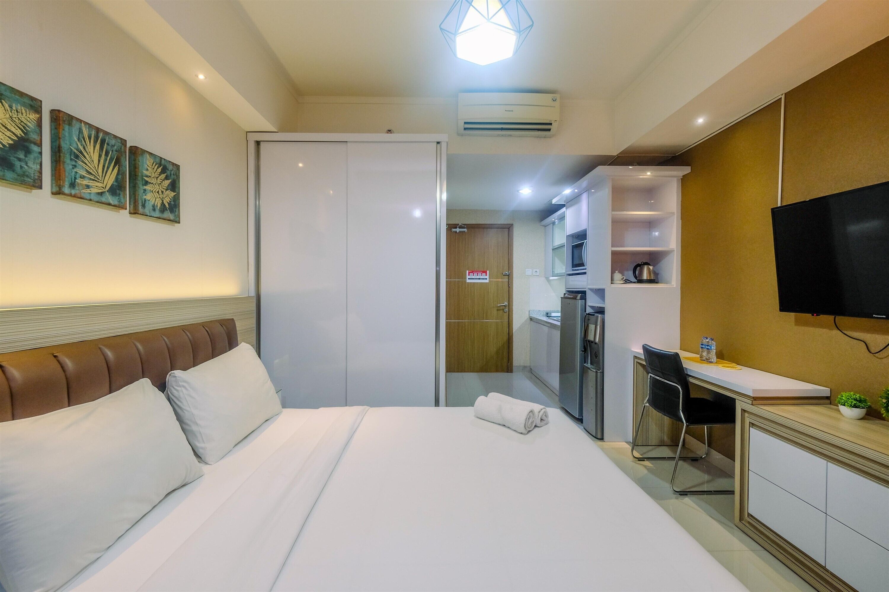 Une chambre d’hôtel équipée d’un lit, d’un bureau, d’une chaise, d’une télévision et d’une kitchenette.