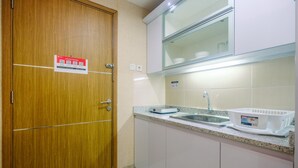A small kitchen with a wooden door, a sink, and a countertop with a dish rack and a box.