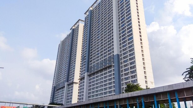 A high-rise building with a modern architectural design, featuring a grid of windows and a prominent central vertical structure. - Homey And Cozy Living Studio Room At Tifolia Apartment (Jakarta)