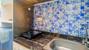 A kitchen with a blue mosaic backsplash, a stainless steel sink, and a black induction cooktop. - Homey And Cozy Living Studio Room At Tifolia Apartment (Jakarta)