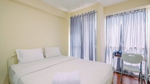 A hotel room with a bed, white bedding, a white towel, a chair, and a window with curtains. - Homey And Cozy Living Studio Room At Tifolia Apartment (Jakarta)