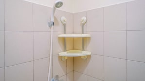 A corner shower with a handheld showerhead and two white shelves. - Homey And Cozy Living Studio Room At Tifolia Apartment (Jakarta)