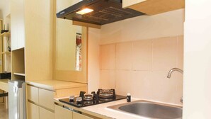 A kitchen with a stainless steel sink, a gas stove, and wooden cabinets. - Homey And Comfort Studio At Tifolia Apartment (Jakarta)