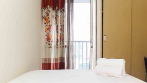 A hotel room with a bed, a door, and a view of the outside. - Homey And Comfort Studio At Tifolia Apartment (Jakarta)