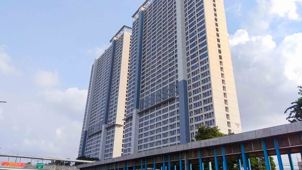 A high-rise building with a modern architectural design, featuring a grid of windows and a prominent vertical structure in the center. - Homey And Comfort Studio At Tifolia Apartment (Jakarta)