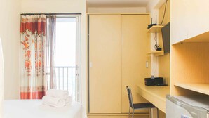 A hotel room with a bed, a desk with a chair, a wardrobe, and a window with curtains. - Homey And Comfort Studio At Tifolia Apartment (Jakarta)
