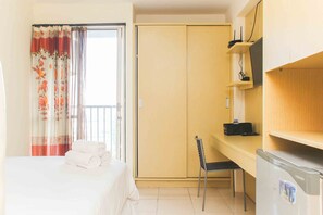 Ein Hotelzimmer mit Bett, Schreibtisch mit Stuhl, Kleiderschrank und einem Fenster mit Vorhängen.