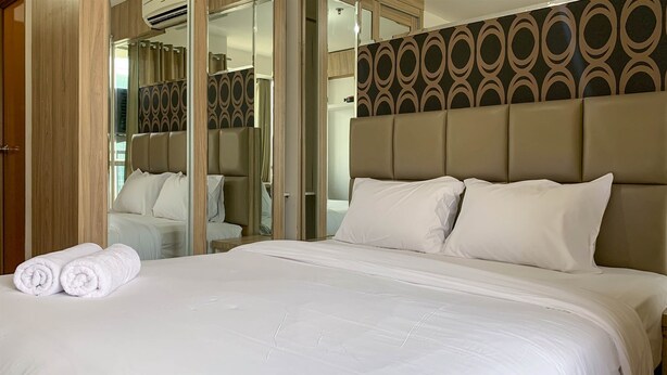 A hotel room with a large bed, a mirror, and a patterned headboard. - Cozy And Tidy Studio At Tifolia Apartment (Jakarta)