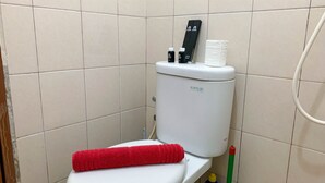 A small bathroom with a white toilet, a red towel on the seat, and a toilet paper holder with two rolls. - Cozy And Tidy Studio At Tifolia Apartment (Jakarta)
