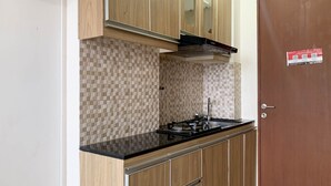 A compact kitchen with a gas stove, a sink, and wooden cabinets. - Cozy And Tidy Studio At Tifolia Apartment (Jakarta)