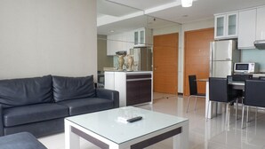 Un salon moderne avec une table basse en verre, un canapé gris foncé et un coin repas comprenant une petite table et des chaises.