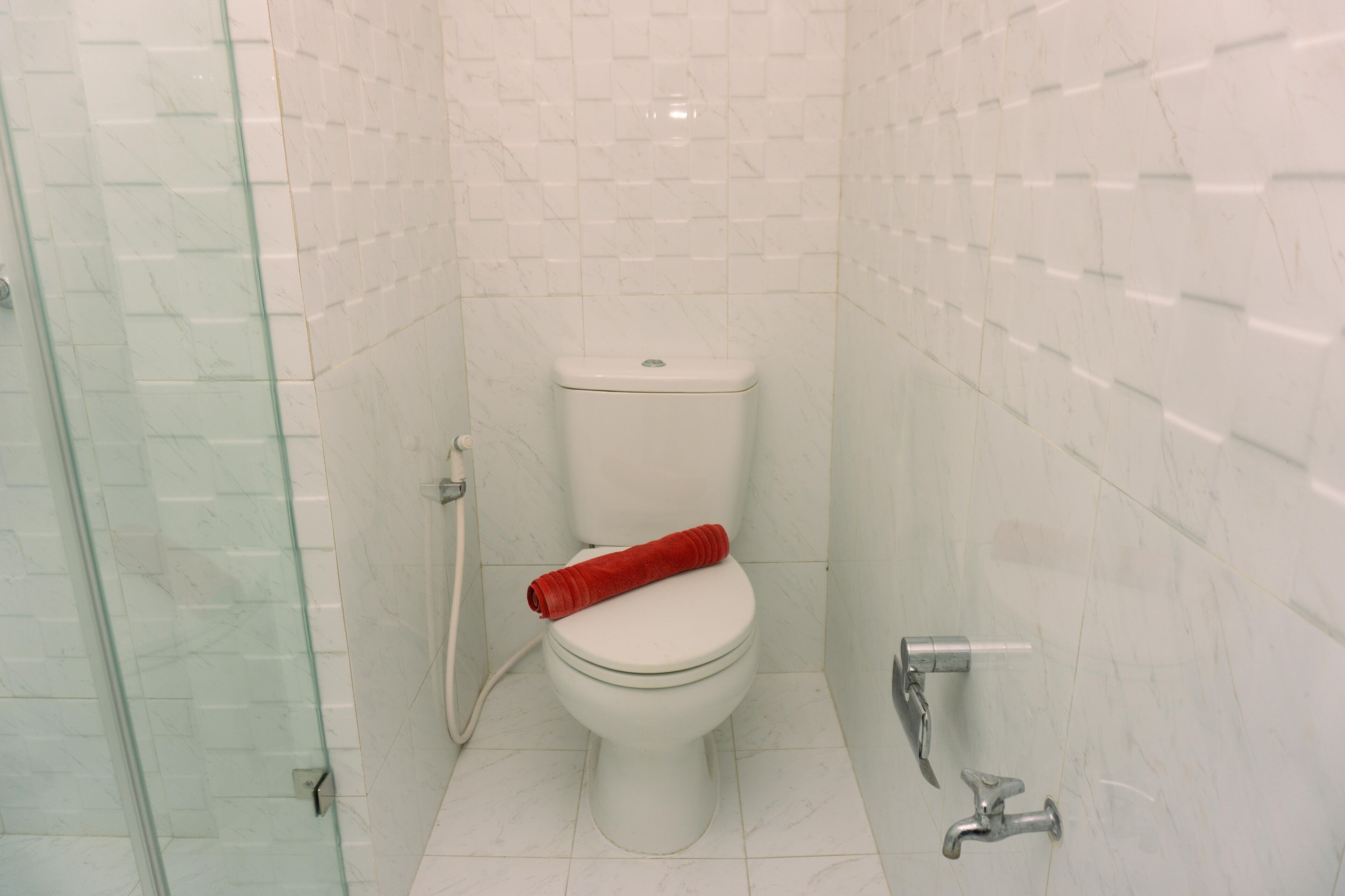 A bathroom with a white toilet, a glass shower enclosure, and a white tiled wall.