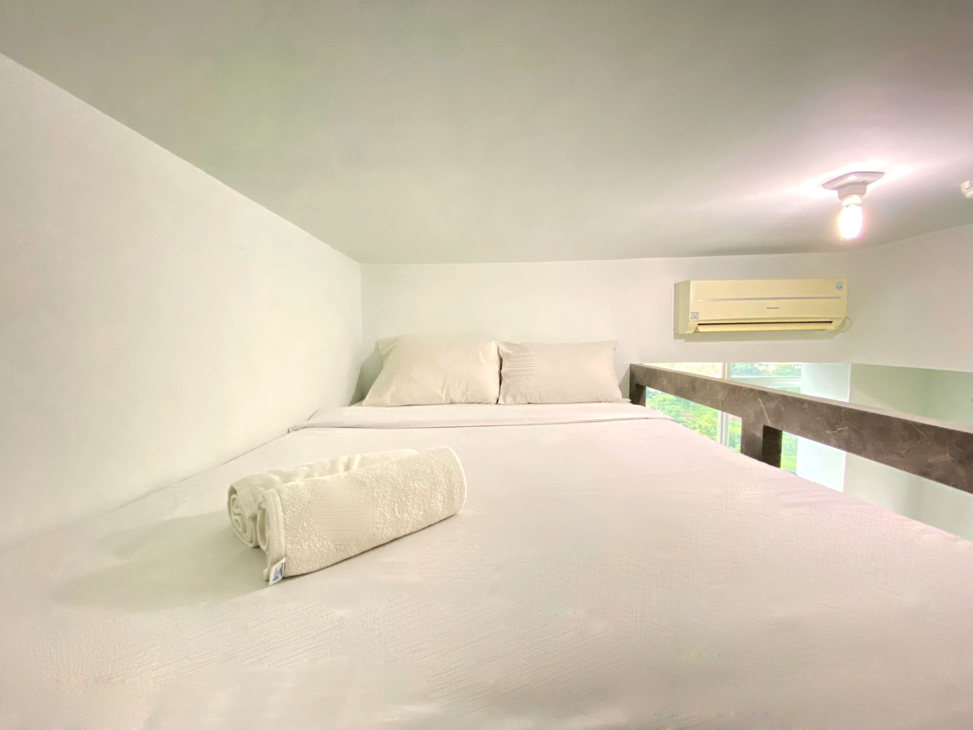 Une chambre à coucher avec un lit, des oreillers, une serviette enroulée, un appareil de climatisation et une fenêtre donnant sur un paysage verdoyant.