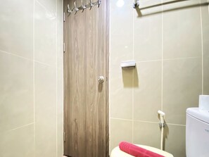 A bathroom with a wooden door, a toilet, and a shower area. - Cozy Studio Room At 12Th Floor Taman Melati Jatinangor Apartment (Hegarmanah)
