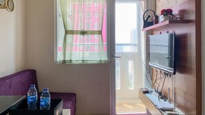 A room with a purple sofa, a table with two water bottles, a TV on a wooden stand, and an air conditioner on the wall. - Modern Look And Comfortable 2Br Green Pramuka City Apartment (Jakarta)