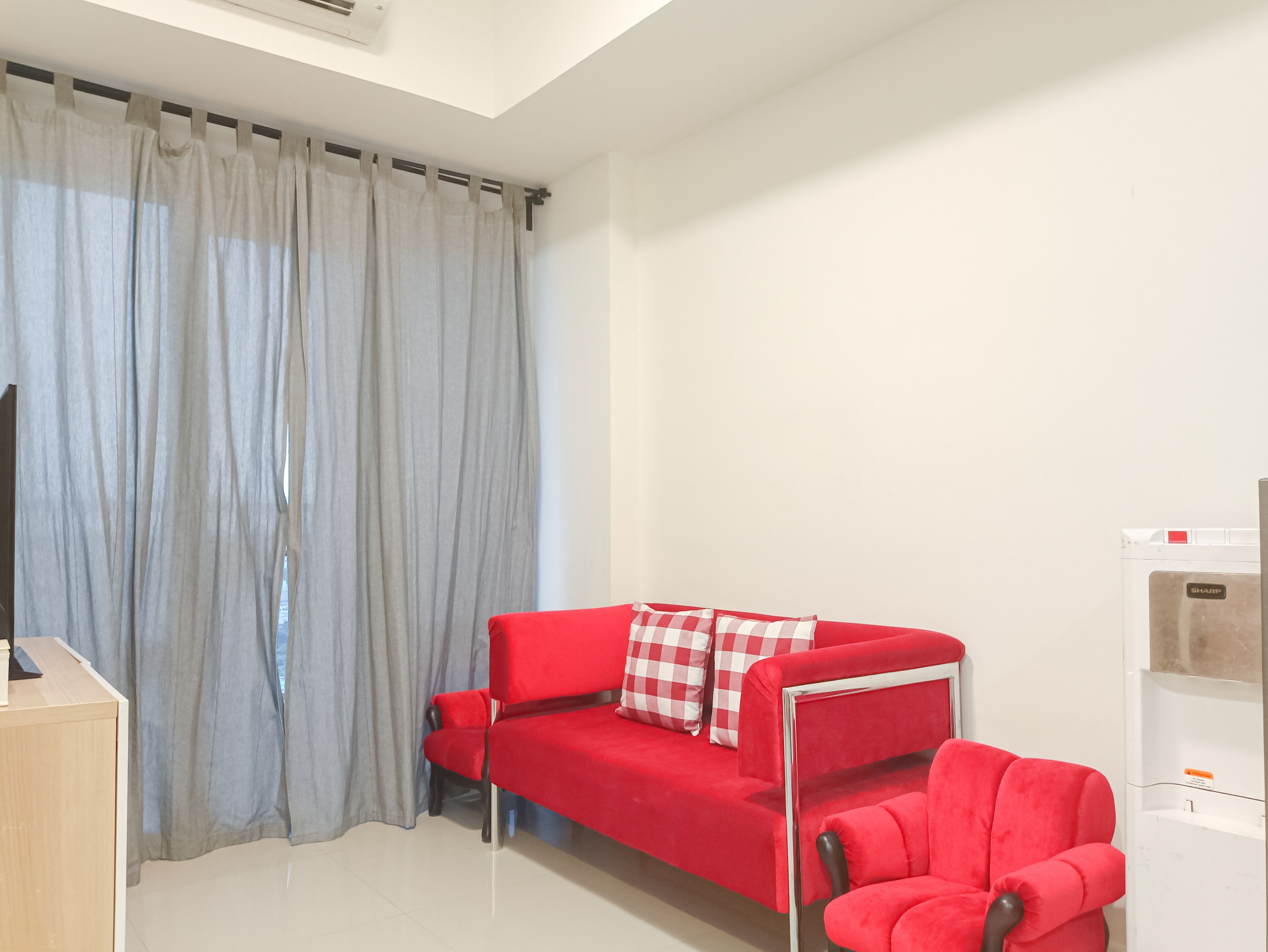 A modern living room with a red sofa, a red armchair, and a television on a wooden stand.