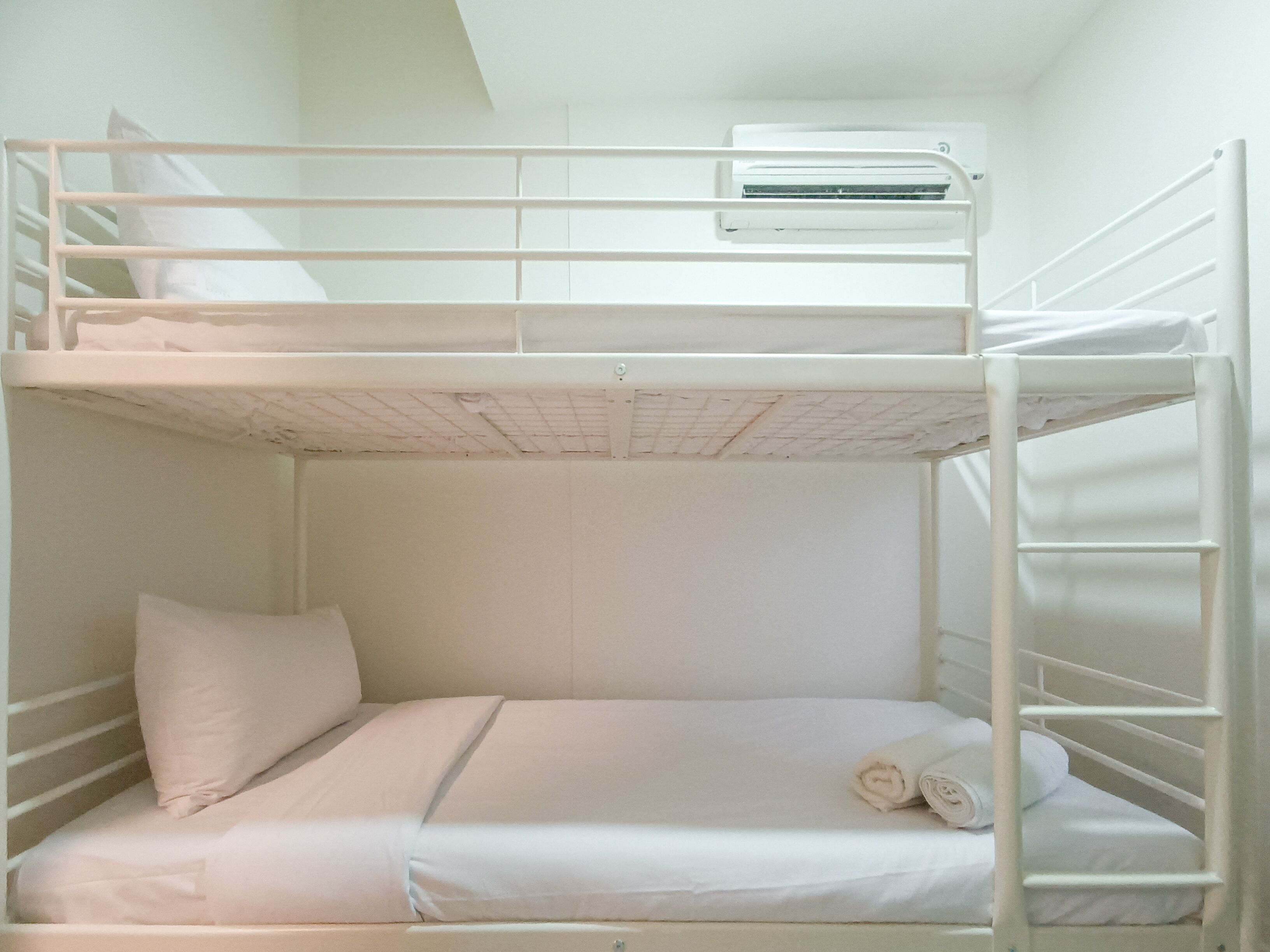 A bunk bed with white bedding and pillows, an air conditioning unit above the top bunk, and a window on the right side.