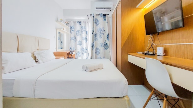 A hotel room with a bed, a desk, a chair, a TV, and an air conditioning unit. - Homey And Elegant Studio Amazana Serpong Apartment (South Tangerang)
