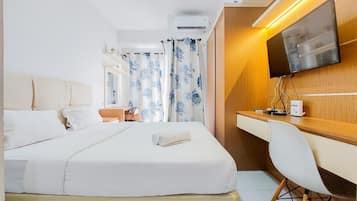 A hotel room with a bed, a desk, a chair, a TV, and an air conditioning unit.