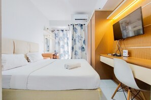 A hotel room with a bed, a desk, a chair, a TV, and an air conditioning unit. - Homey And Elegant Studio Amazana Serpong Apartment (South Tangerang)