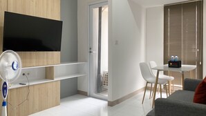 Un soggiorno moderno con TV, una ventola a piantana, una zona pranzo con tavolo e sedie, e una porta scorrevole in vetro che dà su un balcone.