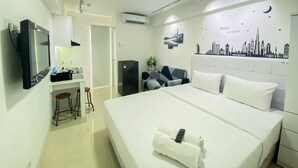 A hotel room with a bed, a desk with a computer, a chair, and a wall with a cityscape mural. - Modern Design And Cozy Studio At Bassura City Apartment (Jakarta)