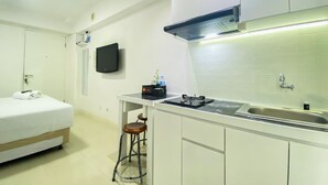 A compact hotel room with a bed, a small kitchenette, a TV mounted on the wall, and a stool. - Modern Design And Cozy Studio At Bassura City Apartment (Jakarta)