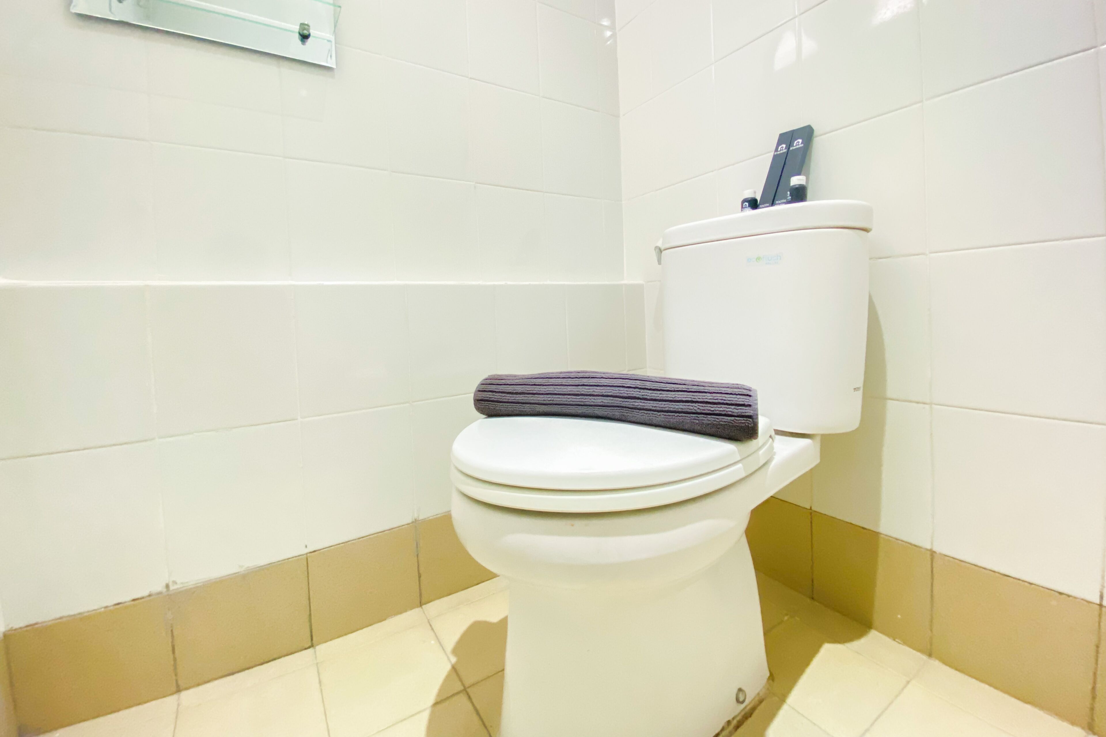 Inodoro con tapa y asiento blancos, una alfombra gris encima y una palanca de descarga a la derecha.