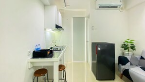 A compact kitchen with a refrigerator, a sink, and a small dining area with stools. - Modern Design And Cozy Studio At Bassura City Apartment (Jakarta)