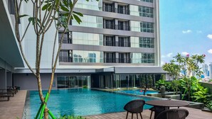 Un bâtiment moderne doté d’une piscine sur le toit, entouré d’une végétation luxuriante et agrémenté de mobilier d’extérieur.
