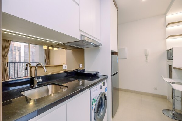 A modern kitchen with a stainless steel sink, a built-in washing machine, and a large window with curtains.